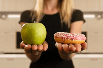 woman's hands holding green apple on the left and donut on the right